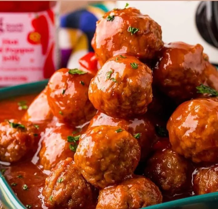 A platter of hot pepper jelly meatballs garnished with herbs.