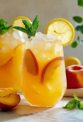 Sweet tart peach lemonade in a glass with fresh peaches and lemons.