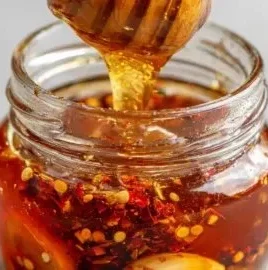 A jar of homemade garlic hot honey with fresh garlic cloves and chili peppers.