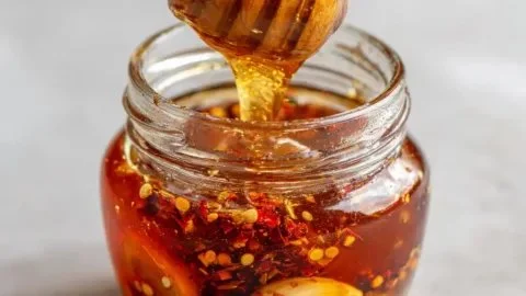 A jar of homemade garlic hot honey with fresh garlic cloves and chili peppers.